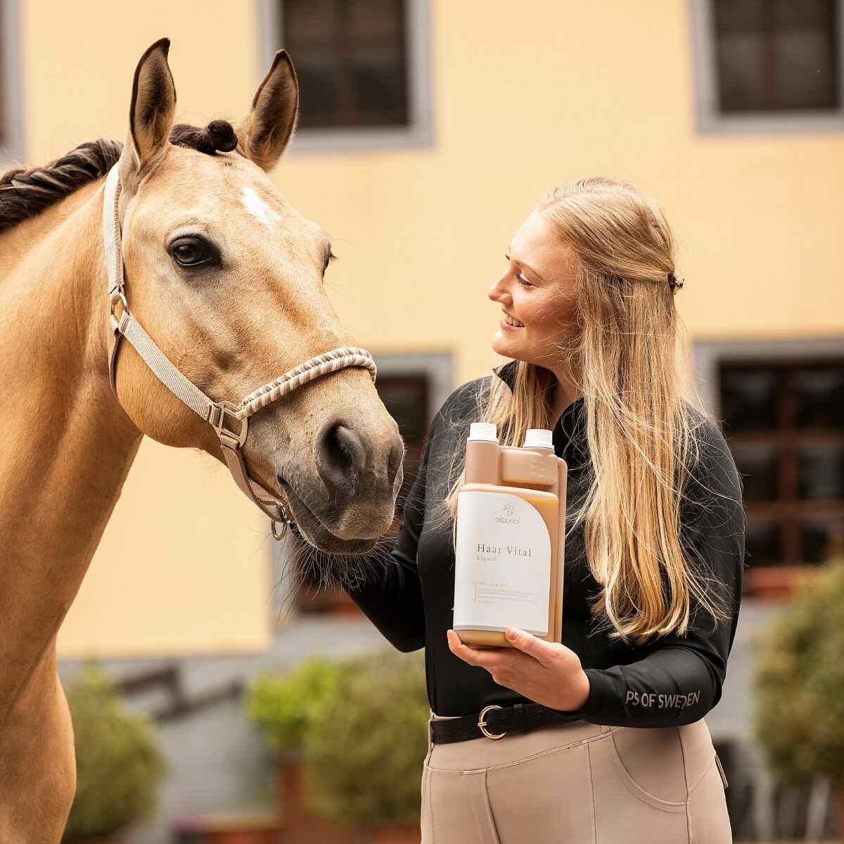 Eine Frau hält eine Flasche Haar Vital von Alpurial neben einem Pferd.